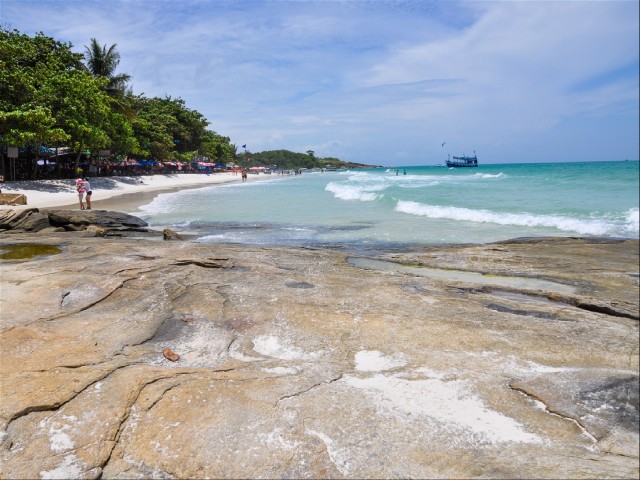 Вид с каменного изгиба берега на пляж с белым песком