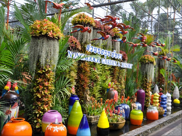 яркие кувшины с фонтанчиками на фоне стены из пальм и растений