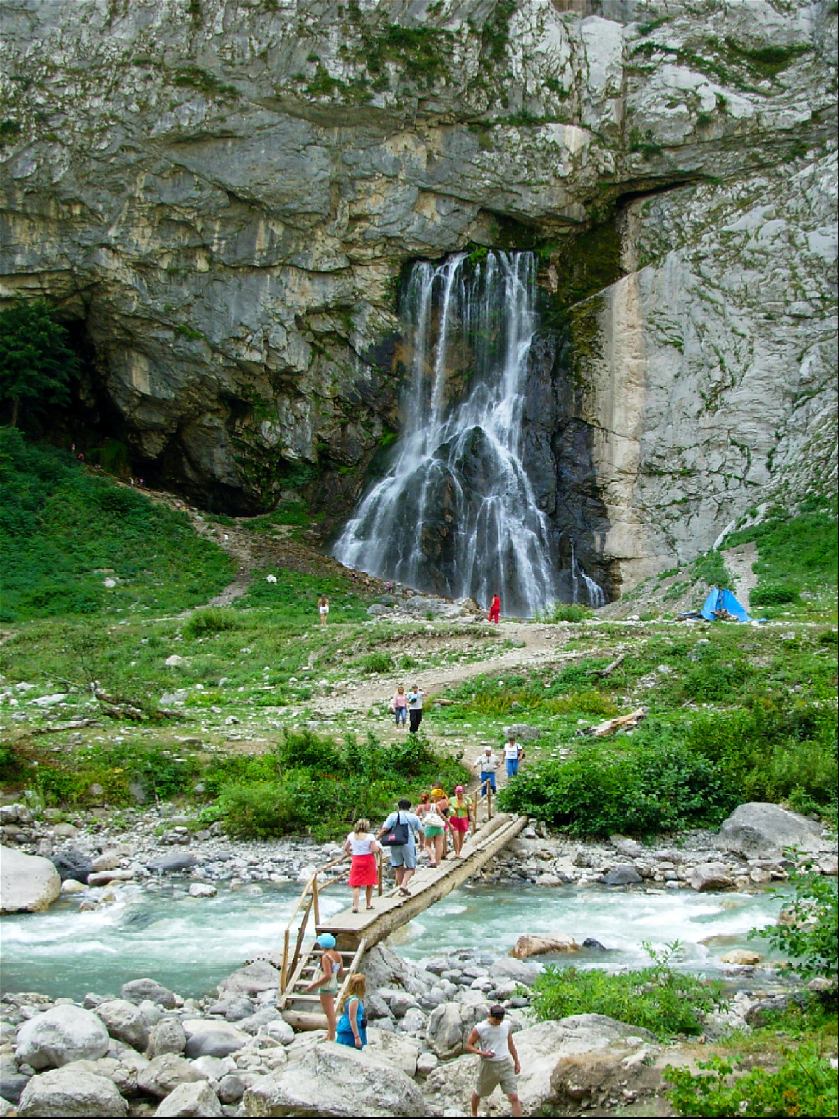 туристы идут по деревянному мостику к водопаду