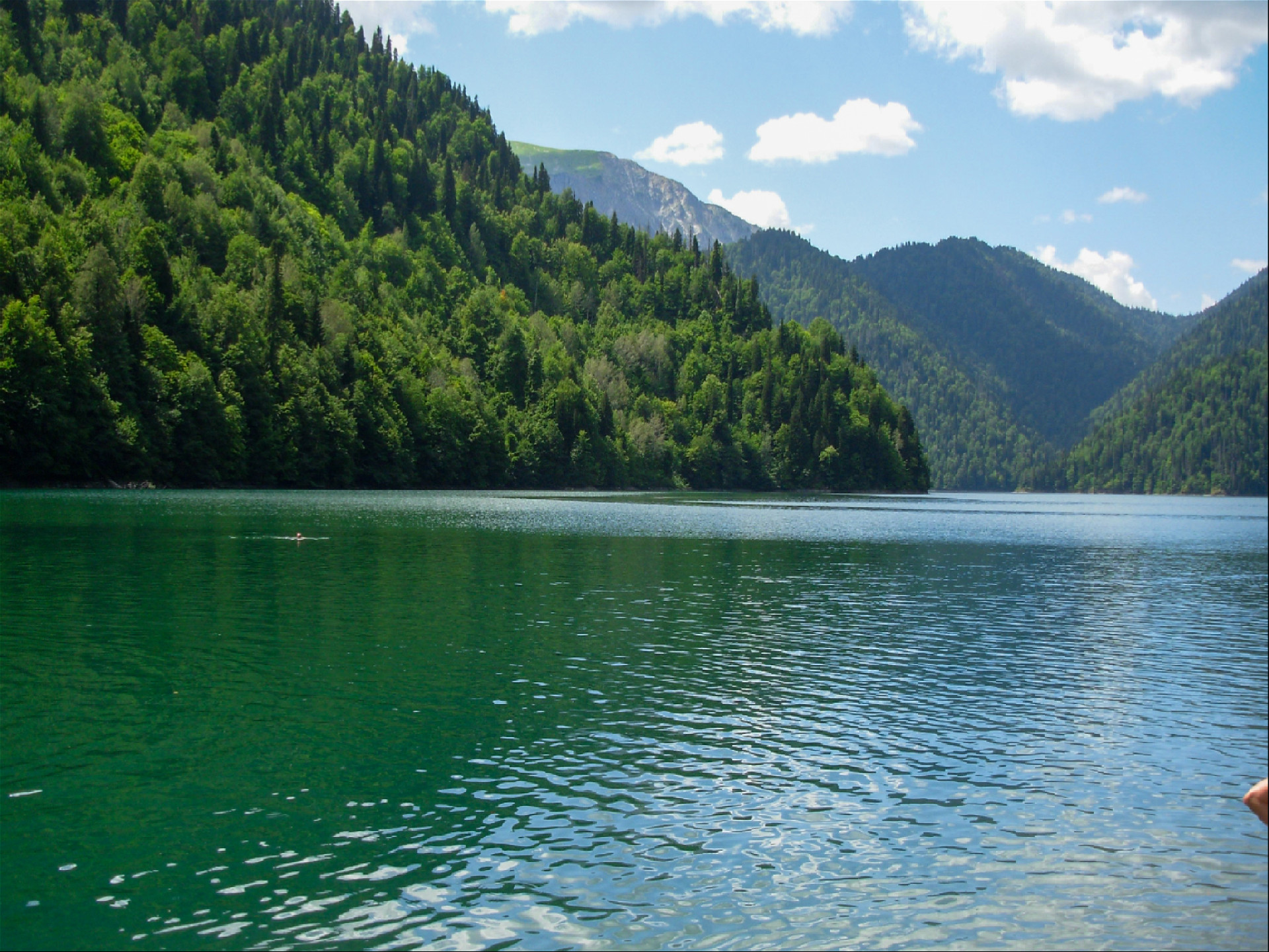 человек купается в озере рица на фоне гор