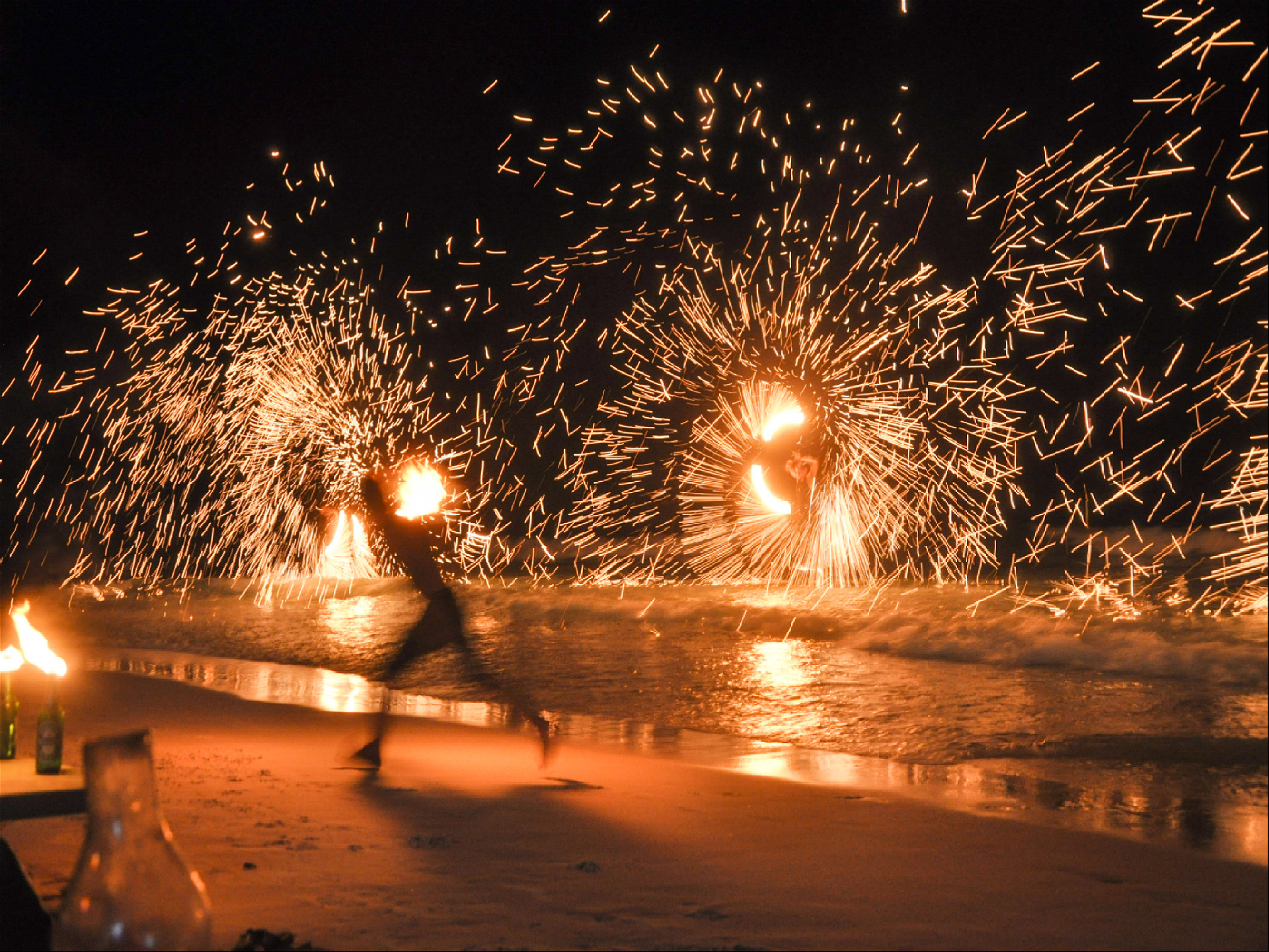 два парня крутят огненные файерболы в волнах прибоя