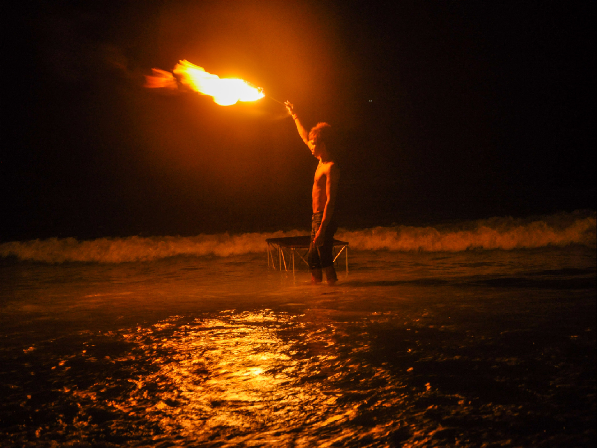 Таец стоит в воде на пляже с факелом в руке