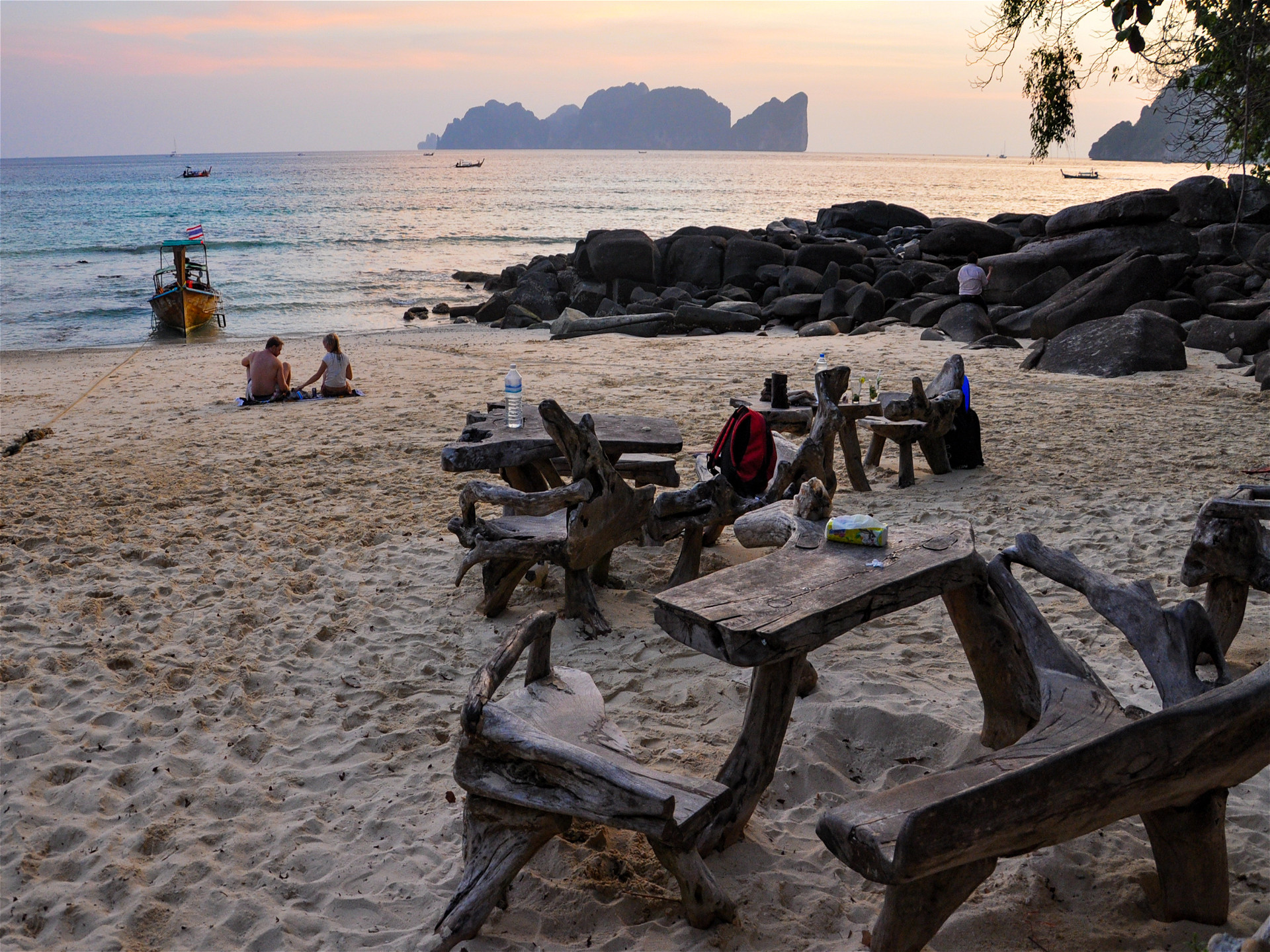 Пляж и деревянные столики на закате с сидящими людьми